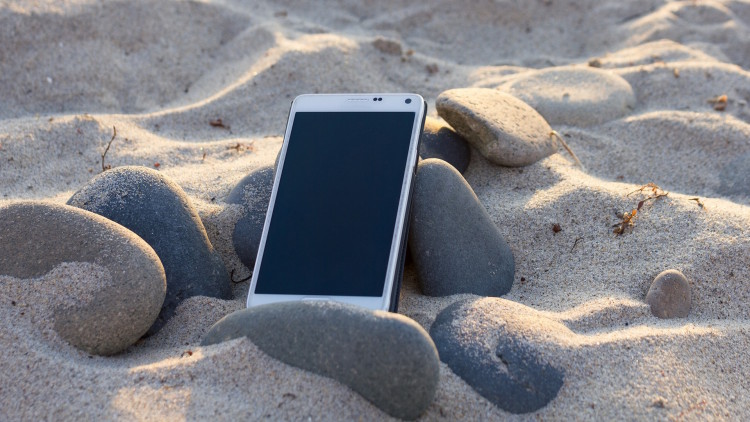 Umfrage: Zwei Drittel der Berufstätigen sind im Sommerurlaub beruflich erreichbar Smartphone im Sand